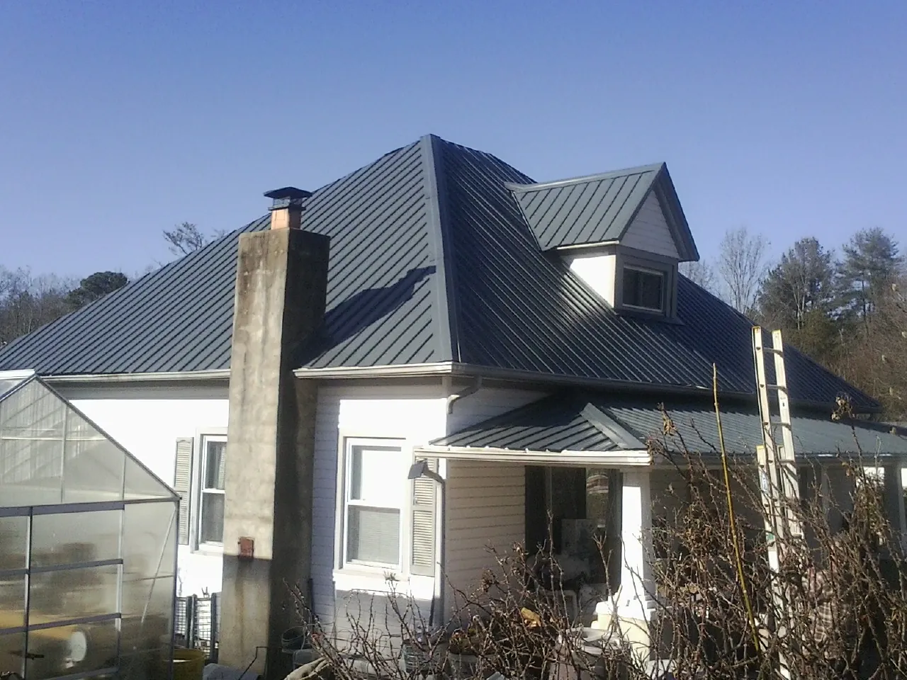 Dark blue standing seam metal roof on a white farmhouse with dormer — Slate & Tile Roof Repair by Roofing Brothers in Fulton